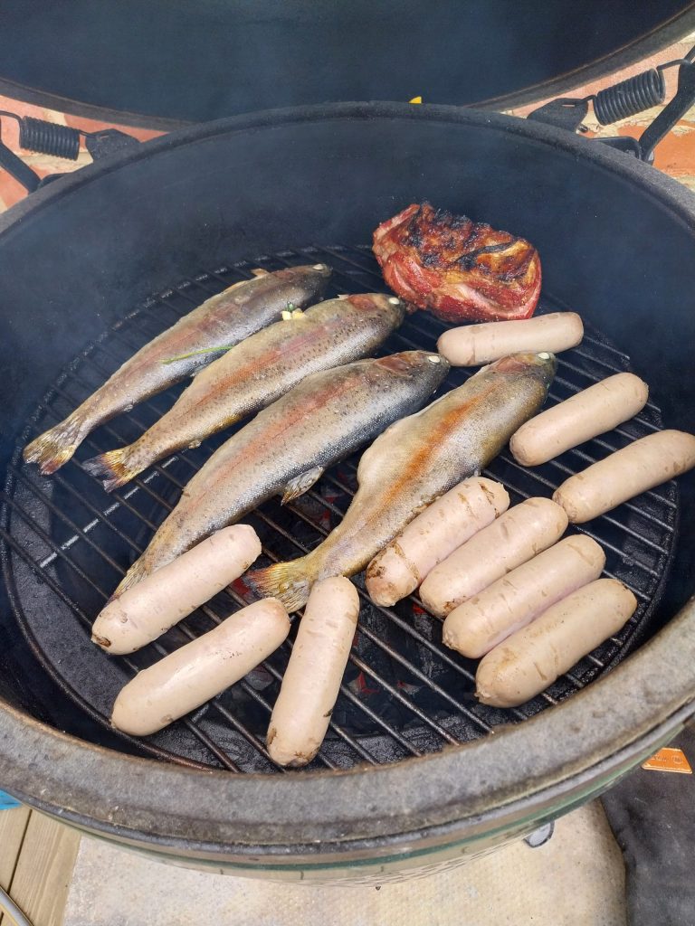 Four whole trout, a lamb rump and sausages filling the rest of a Big Green Egg Large's 46cm grid.