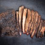 A smoked brisket sliced on a dark board, from Bromfields' packer cut listing.