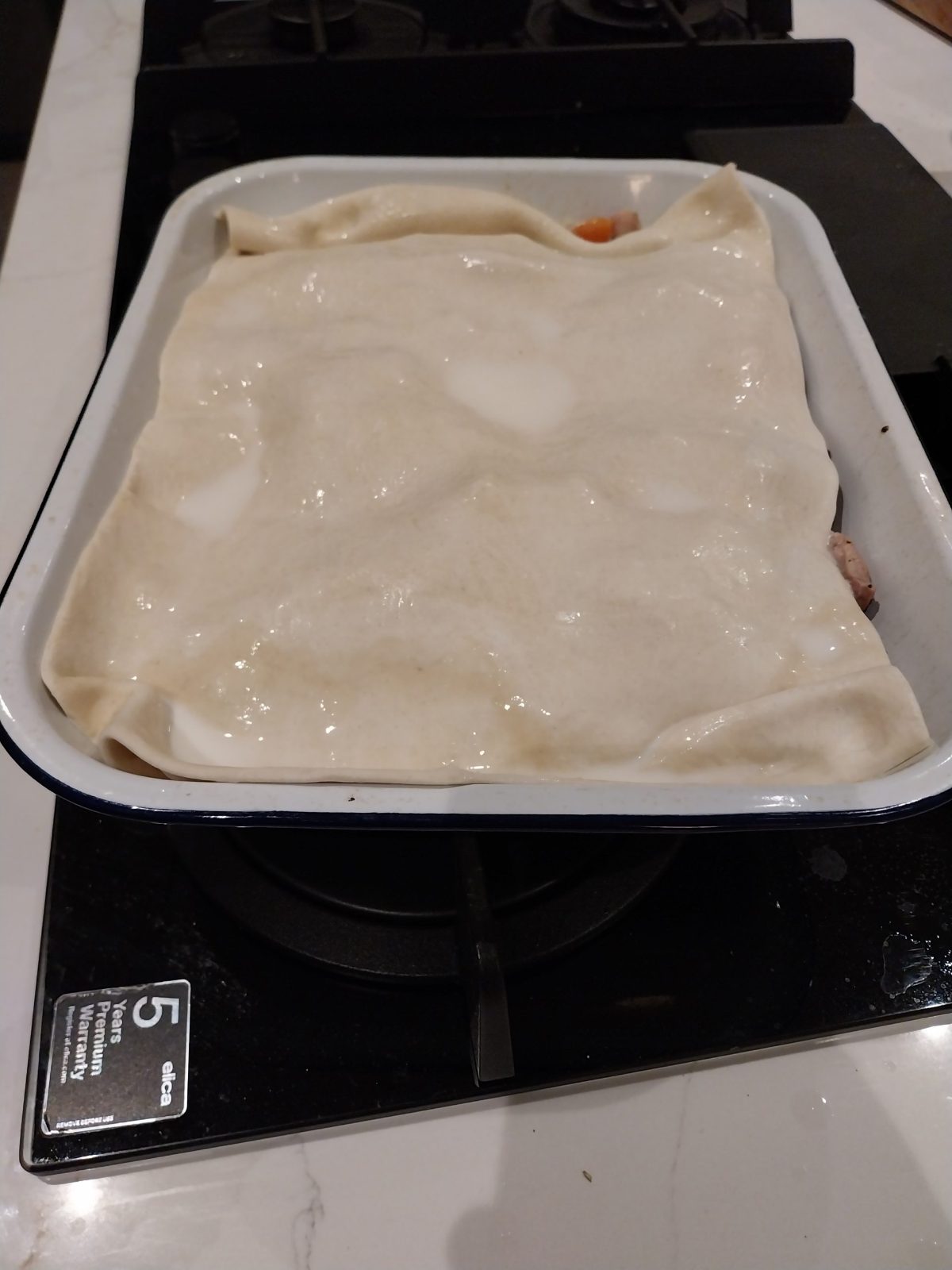 A sheet of puff pastry draped over the pie dish and brushed with milk