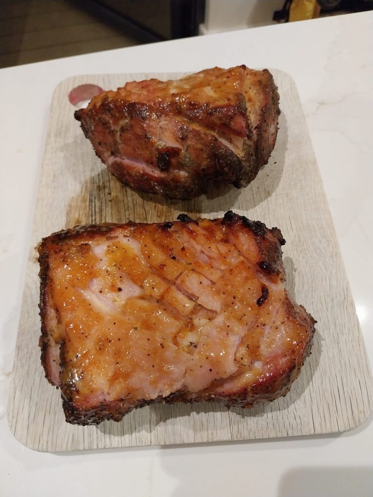 Two glazed gammon joints on a wooden board, the fat scored and coated in an orange glaze