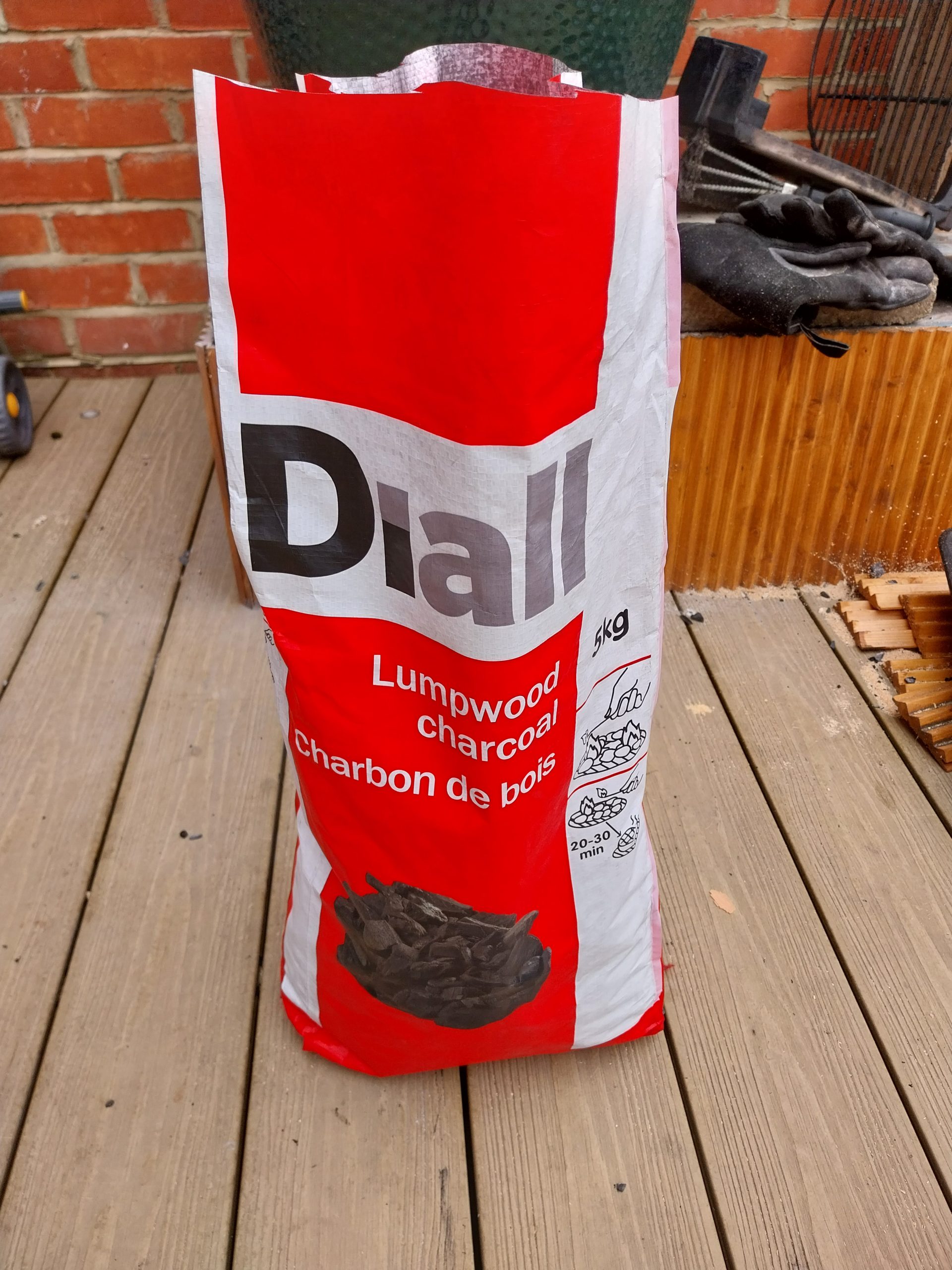 A 5kg bag of Diall lumpwood charcoal from B&Q, standing on the decking by the Big Green Egg