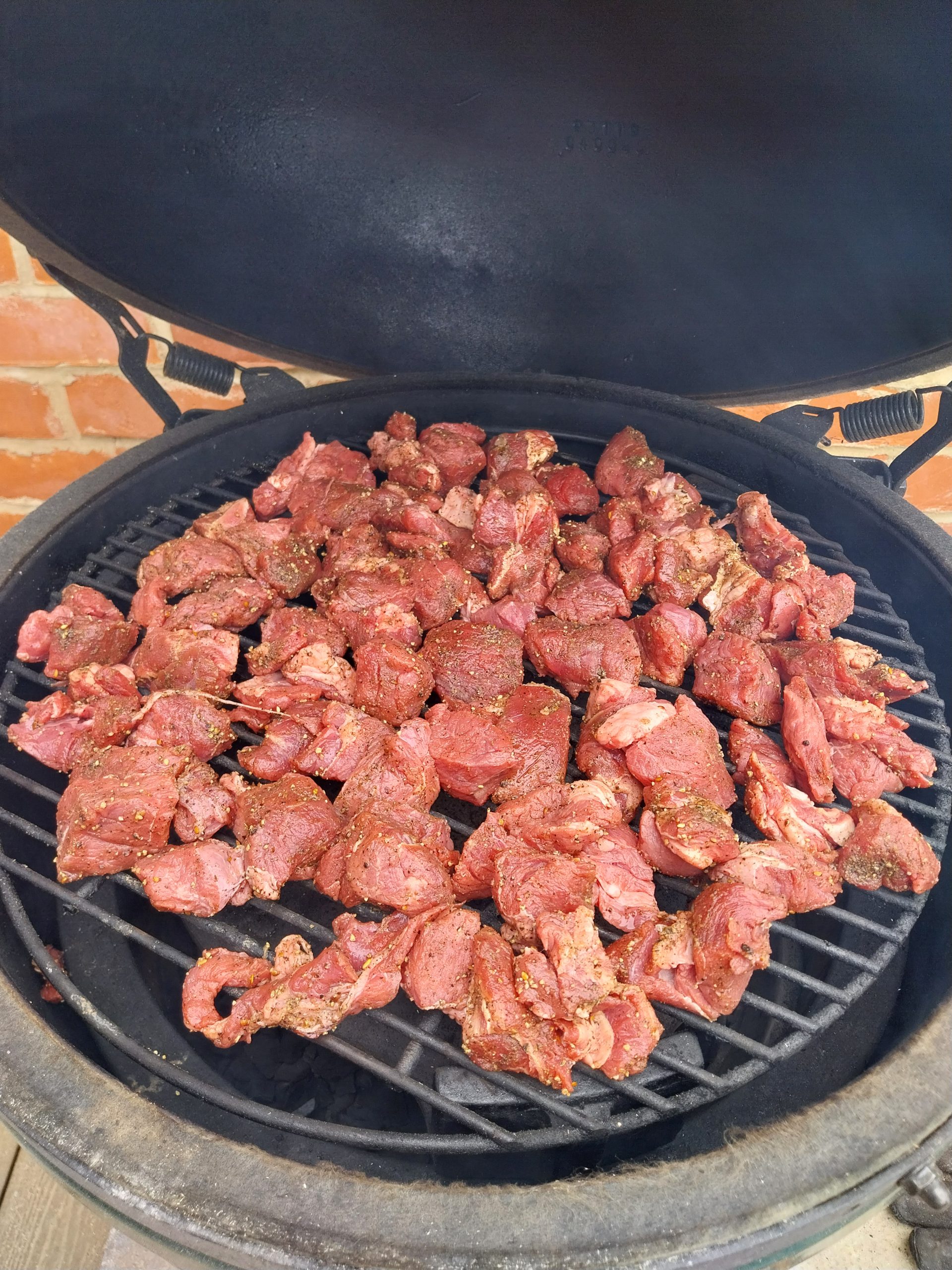 Diced beef chuck seasoned with salt, pepper and garlic, spread out on the grid of the Big Green Egg with the lid open