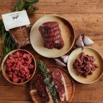 Grass-fed beef laid out on a wooden table: a rolled joint, mince, diced beef and two steaks, with a pouch of gravy, from Edenmoor's Grass Fed Beef Box listing.