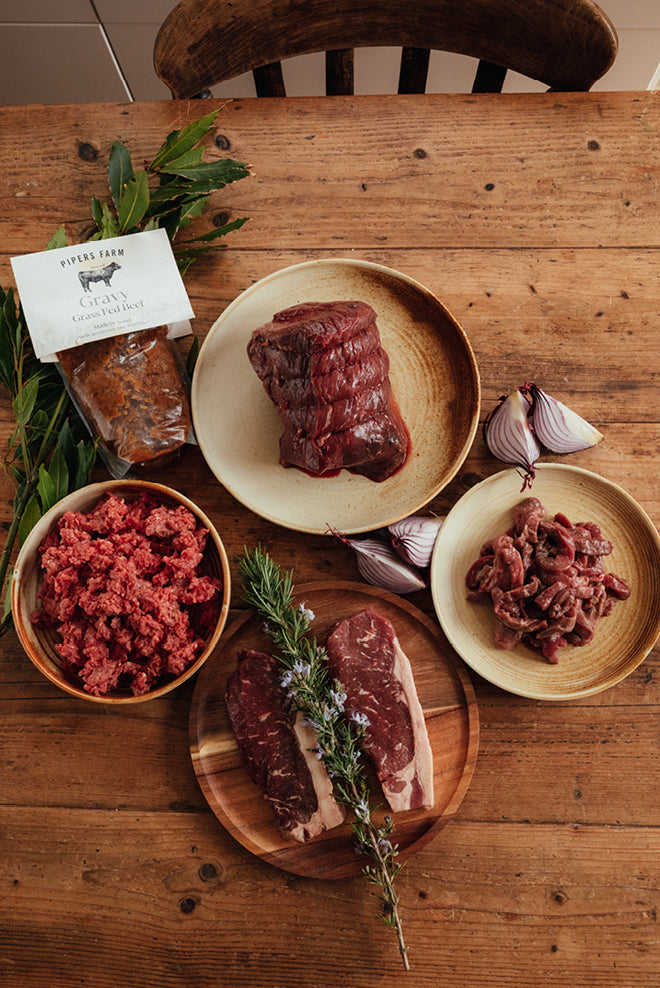 Grass-fed beef laid out on a wooden table: a rolled joint, mince, diced beef and two steaks, with a pouch of gravy, from Edenmoor's Grass Fed Beef Box listing.