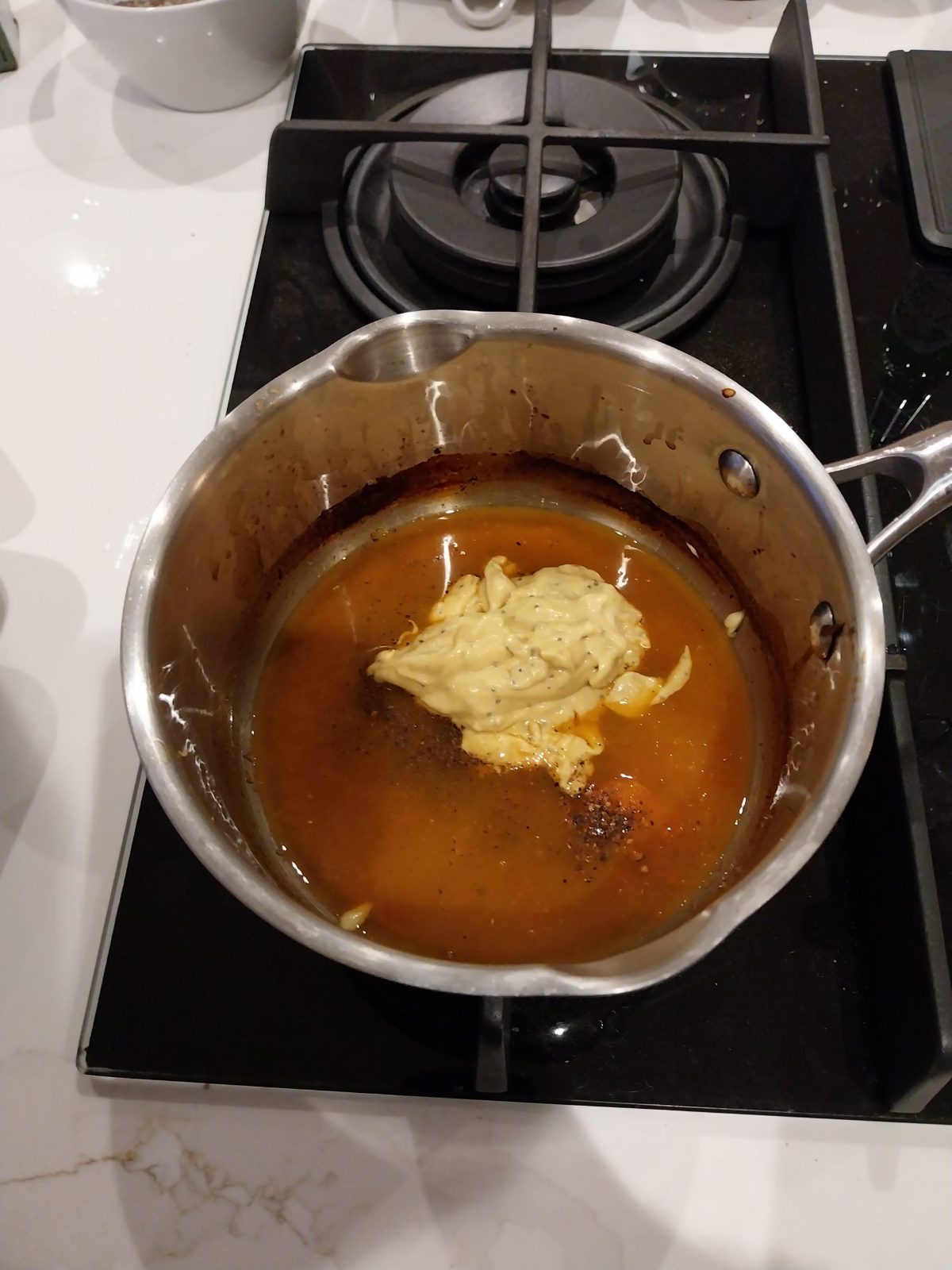 Dijon mustard and black pepper going into reduced grapefruit juice in a saucepan on the hob