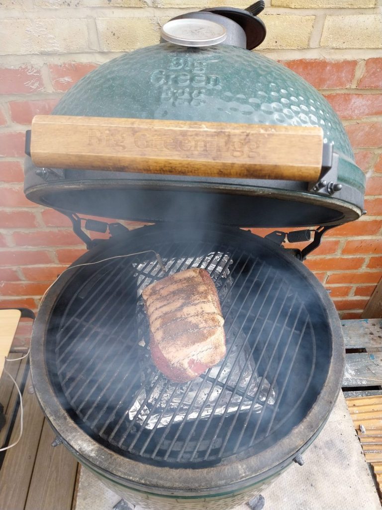 A gammon joint with the rind and string on, on the grid of a Big Green Egg with the lid open