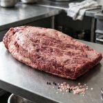 A raw whole brisket on a steel butcher's bench, from Grid Iron Meat's listing.