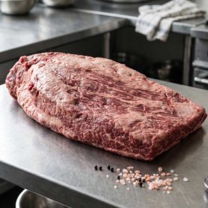 A raw whole brisket on a steel butcher's bench, from Grid Iron Meat's listing.