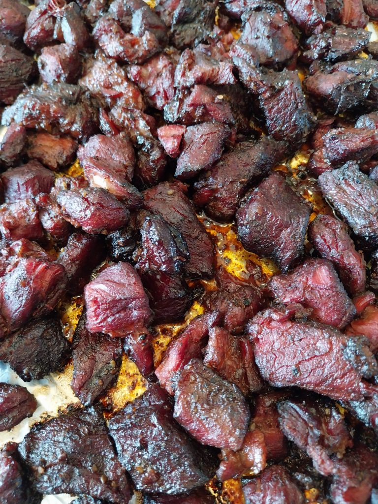 Beef chuck burnt ends finished and glazed, dark and sticky in a foil-lined tray, coming off the Big Green Egg