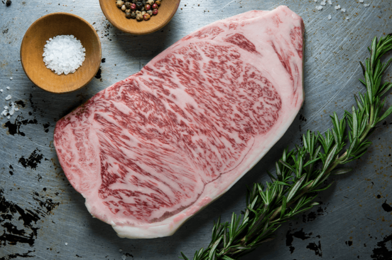 A raw A5 Japanese Wagyu sirloin steak, heavily marbled, on a dark board with rosemary, salt and peppercorns, from Tom Hixson's listing.