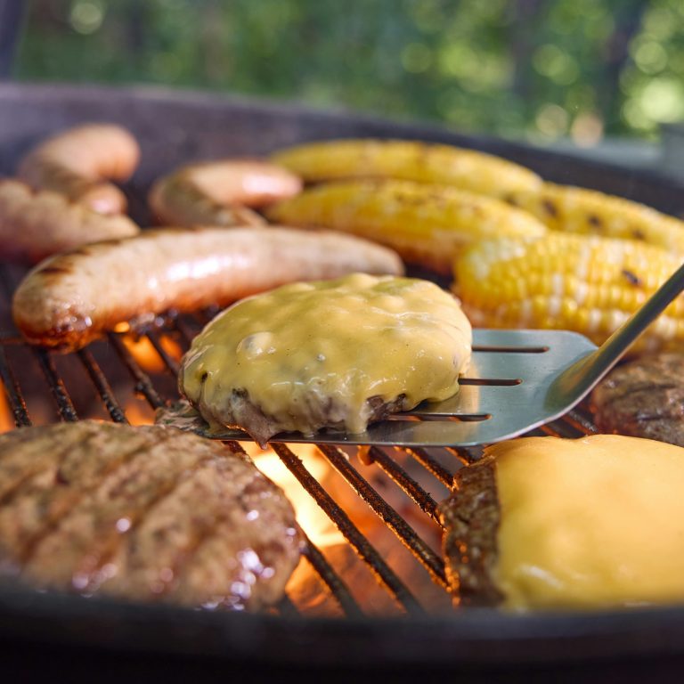 Sausages, burgers and corn on the cob over hot coals on a Weber kettle grate