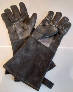 My WZQH leather gloves, a well-used black suede pair with long cuffs, scuffed grey across the palms and fingers, on a white worktop.